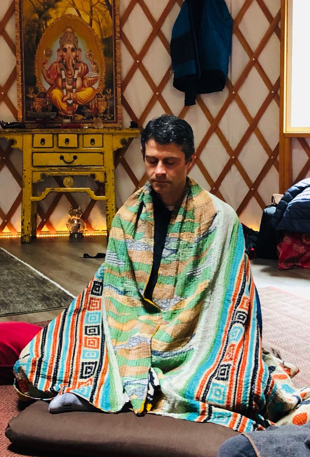 Chad seated with his eyes closed in meditation, wrapped in a colorful blanket.
