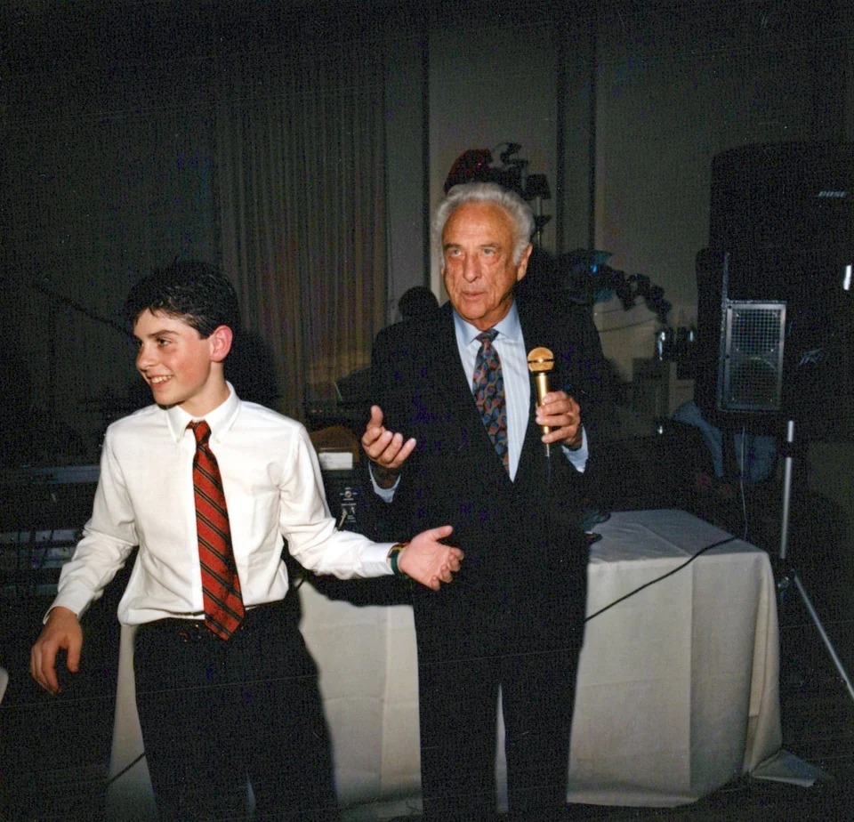 Chad beside his grandfather, who is holding a microphone at Chad’s bar mitzvah.