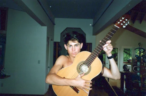 Chad as a teenager at home, holding an acoustic guitar.